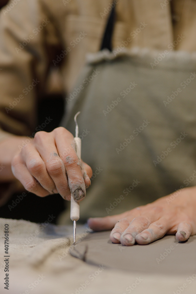 Obraz premium beautiful women hands cut off the edge of a piece of clay to make a plate with their hands. Creative master class in the pottery workshop