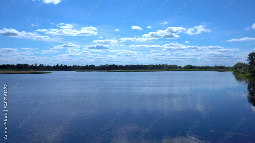 Clouds are reflected in the lake. View of the lake in the distant grass and clouds