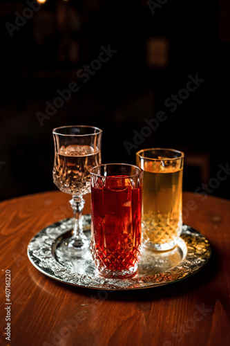 Two long drink cocktails with ice in vintage highball glasses and a glass of wine or vermouth on a silver tray