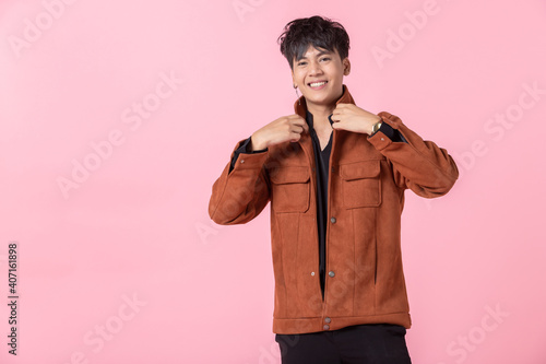 fashion Portrait of Confident handsome young Asian man with keeping hands in pockets of pocket the side eyes looking at camera in isolated on pink blank copy space studio background. © Thinapob