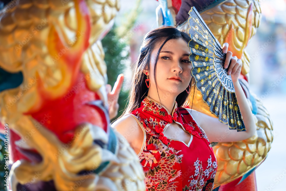 Portrait beautiful smiles Asian young woman wearing red traditional Chinese cheongsam decoration and holding a Chinese Fanning for Chinese New Year Festival at Chinese shrine in Thailand