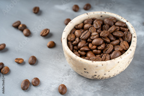 Fototapeta Naklejka Na Ścianę i Meble -  Сoffee beans in a ceramic bowl - selective focus. Scattered coffee beans on a gray background. High quality photo