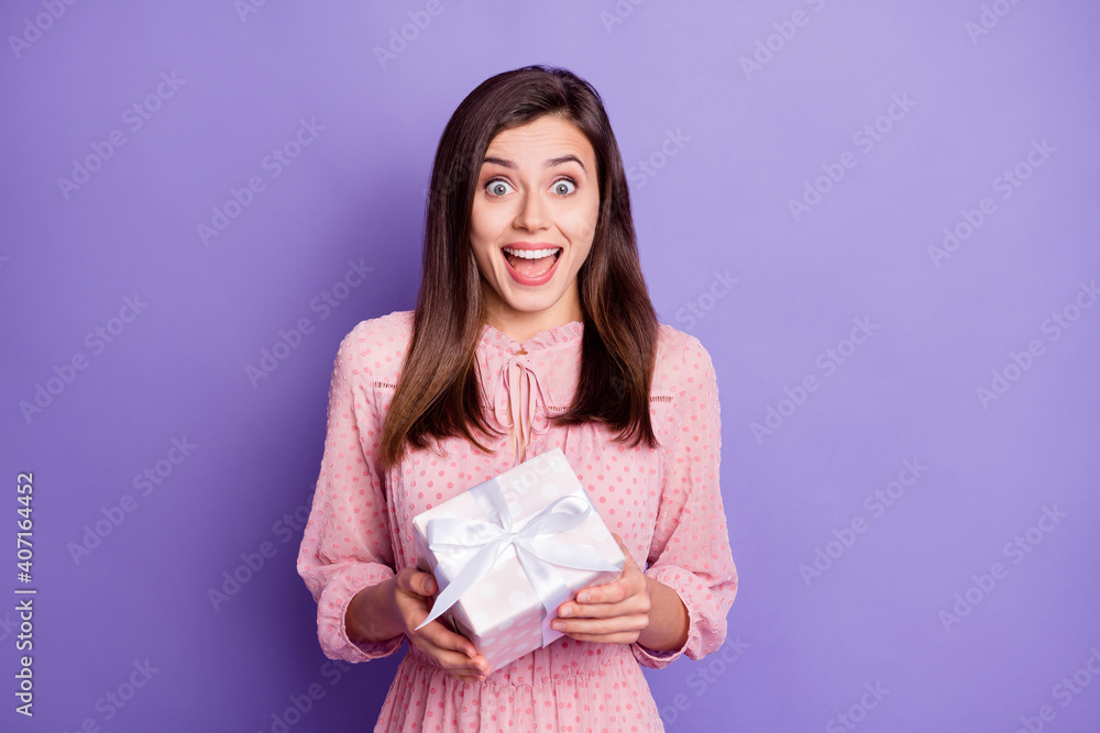 Portrait of attractive amazed cheerful girl holding in hands white giftbox isolated over bright violet color background Portrait of attractive amazed cheerful girl holding in hands white giftbox isolated over bright violet color background