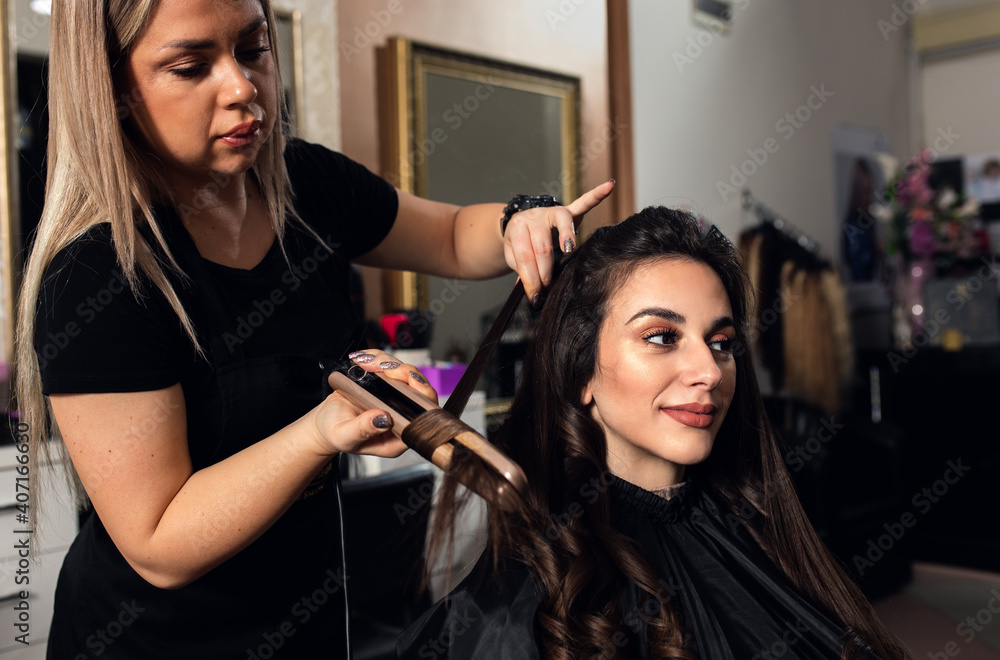 Female hairdresser makes hairstyle on young woman with brunette hair in salon. Female hairdresser makes hairstyle on young woman with brunette hair in salon.