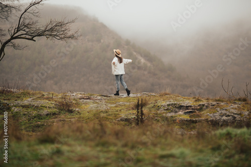 Cloudy weather, calm atmosphere. The happy girl with hands up travels through the mountains. 
