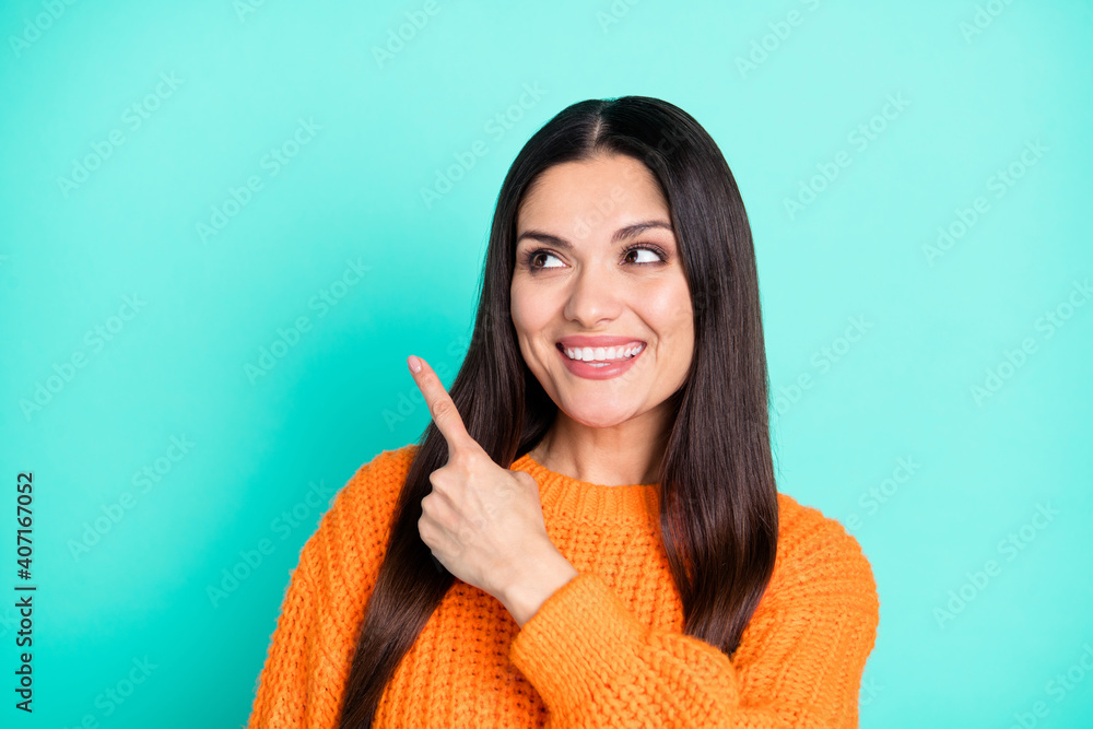 Photo of positive woman direct finger look empty space wear orange sweater isolated teal color background Photo of positive woman direct finger look empty space wear orange sweater isolated teal color background