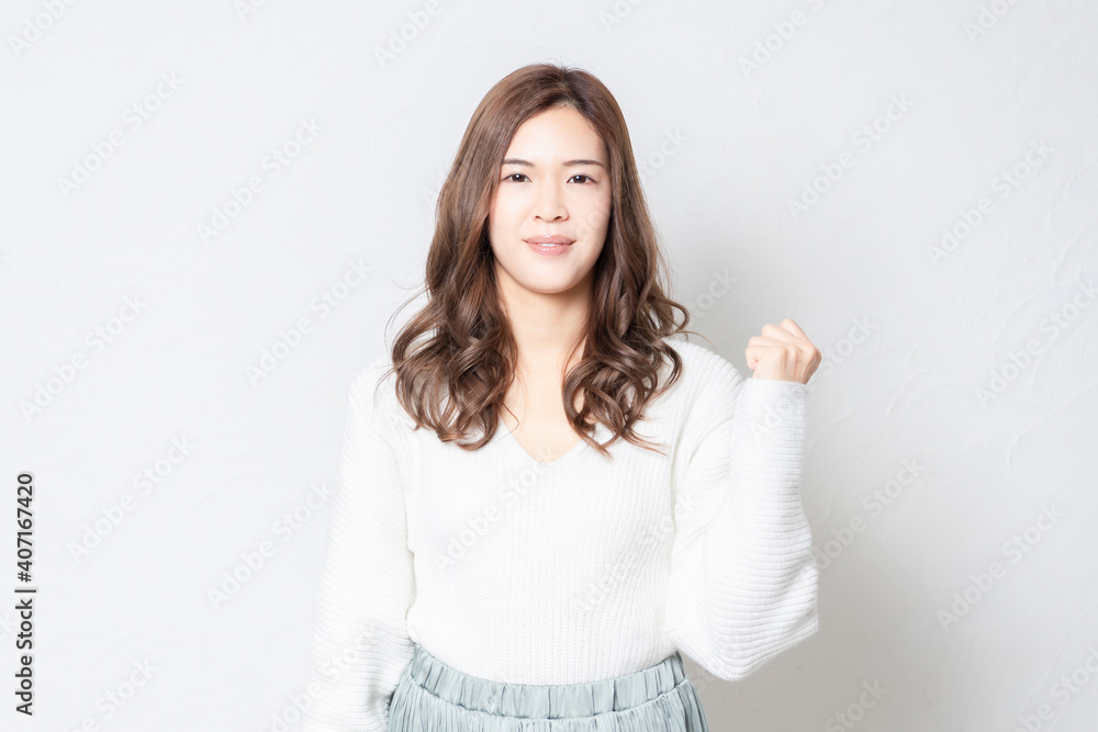 白い壁の前でガッツポーズをする若い女性 白い壁の前でガッツポーズをする若い女性