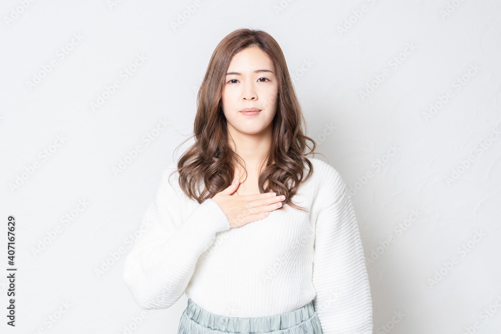 白い壁の前に立って胸に手を当てる若い女性 白い壁の前に立って胸に手を当てる若い女性