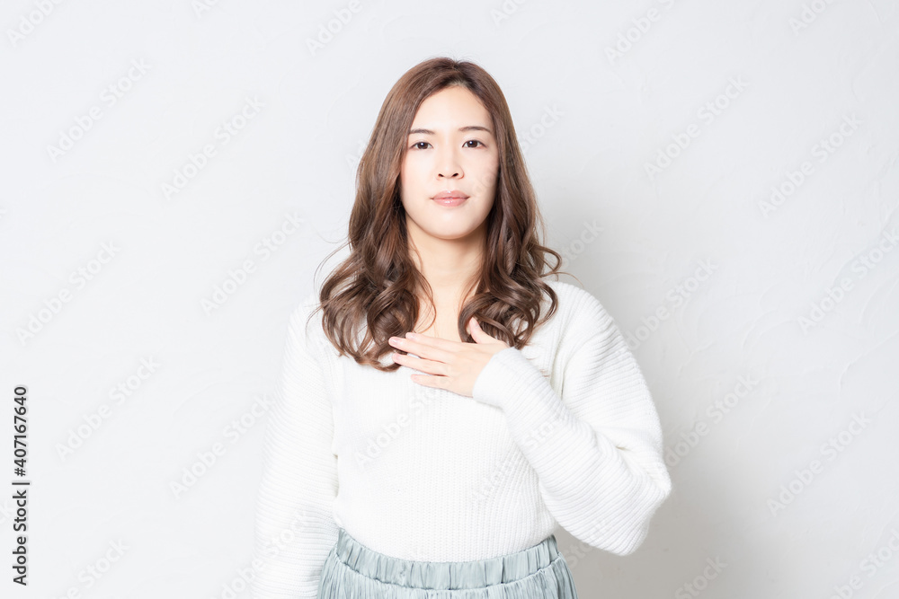 白い壁の前に立って胸に手を当てる若い女性 白い壁の前に立って胸に手を当てる若い女性