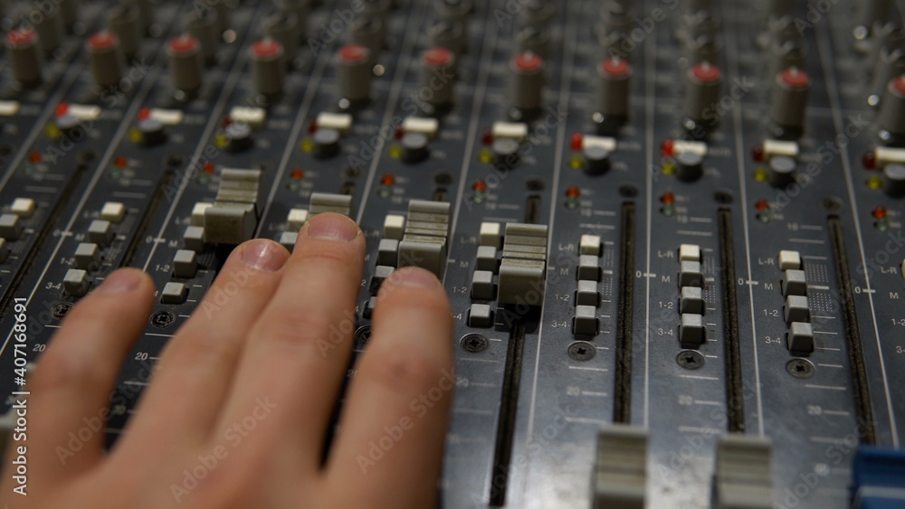 The man adjusts the sound using the sliders on the panel. Mixer for controlling and adjusting sound. Old specialized professional equipment.