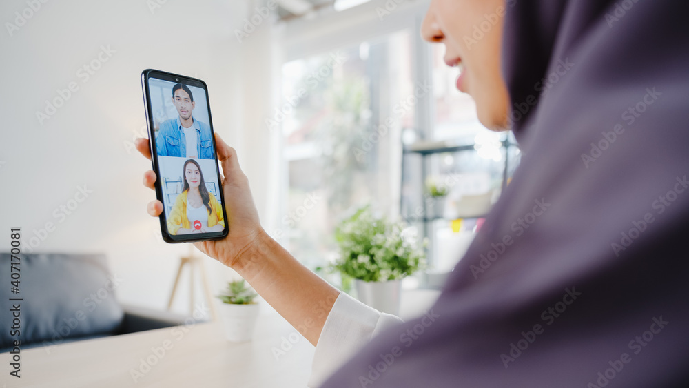 Young Asia muslim businesswoman using smart phone talk to colleague by videochat brainstorm online meeting while remotely work from home at living room. Social distancing, quarantine for corona virus. Young Asia muslim businesswoman using smart phone talk to colleague by videochat brainstorm online meeting while remotely work from home at living room. Social distancing, quarantine for corona virus.