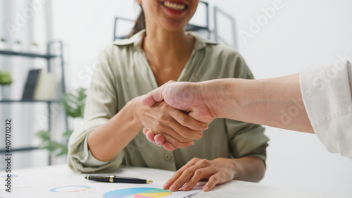 Multiracial group of young creative people in smart casual wear discussing business shaking hands together and smiling while sitting in modern office. Partner cooperation, coworker teamwork concept.