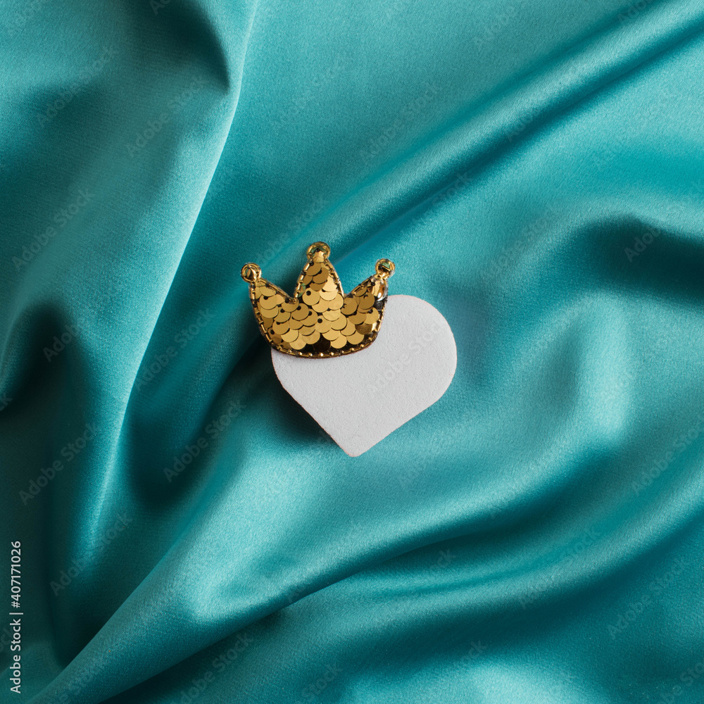 Pink heart with a golden crown on a green background. Flat lay