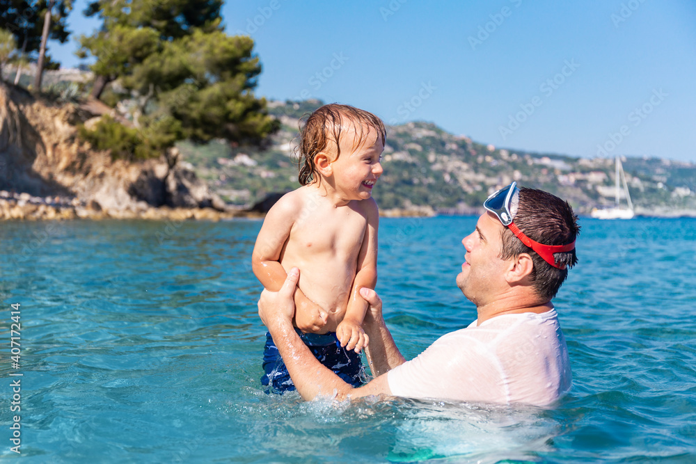 Father and little son having fun swimming and playing together in sea water at summer holidays. Family bonding, togetherness. Seaside vacation.