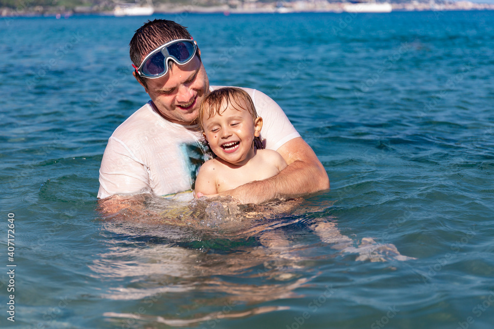 Father and little son having fun swimming and playing together in sea water at summer holidays. Family bonding, togetherness. Seaside vacation. Father and little son having fun swimming and playing together in sea water at summer holidays. Family bonding, togetherness. Seaside vacation.