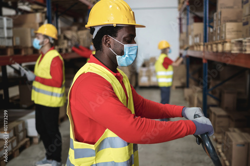 African warehouse worker loading delivery boxes while wearing safety mask - Focus on face