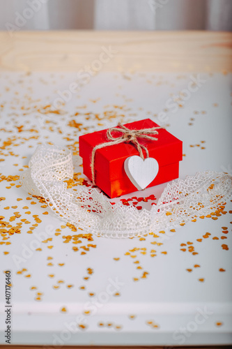 Small red gift box with golden glitters around. Red present with heart on the rope on white background. Saint Valentine's Day present. Heart-shaped golden glitters.