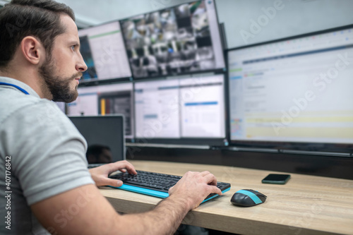 Attentive man with keyboard in front of computer screens