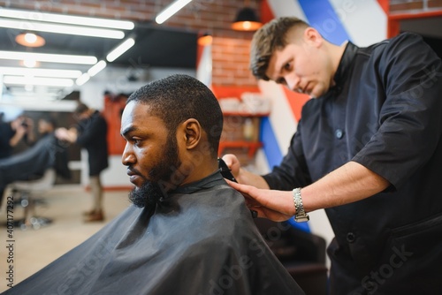 Closeup of process of trimming of hair in barber shop. Qualified barber keeping clipper in hands and correcting shape of hair to male client sitting on chair. Concept of haircut and shaving.