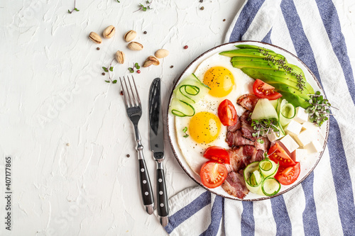 Healthy nutritious paleo keto breakfast with egg, bacon, avocado, cheese and fresh salad on white plate on light background. Flat lay