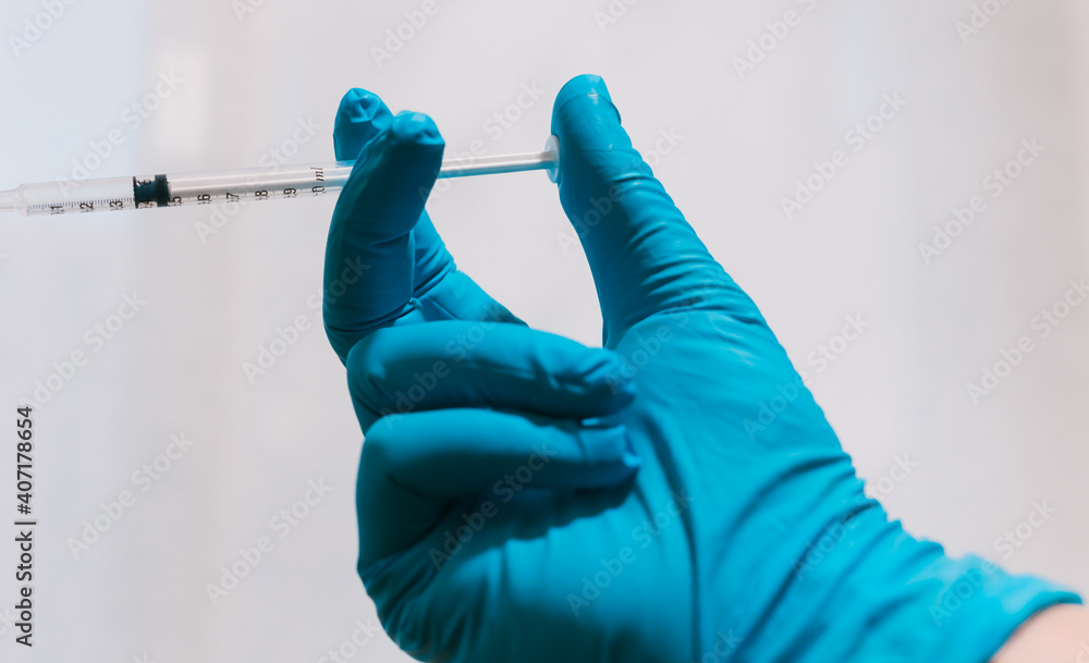 You can see a full hand with a blue glove, holding a syringe. You can see a full hand with a blue glove, holding a syringe.