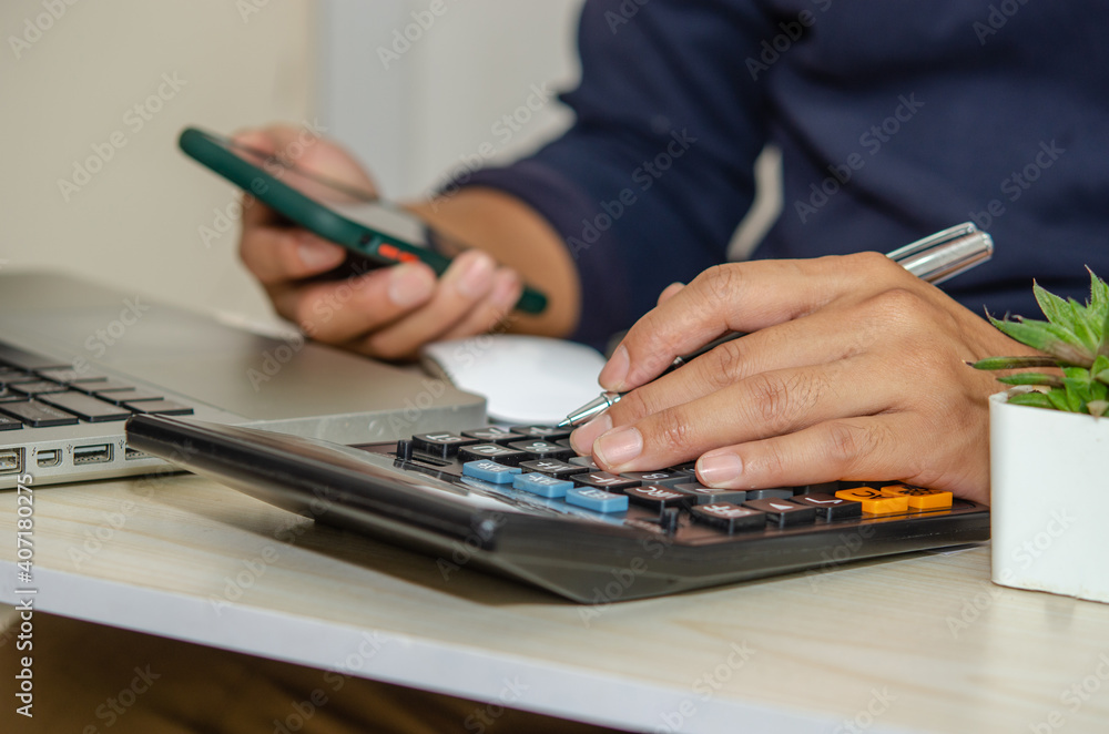 custom made wallpaper toronto digitalbusinessman using a calculator holds a pen and a mobile phone on a desk with a laptop work from home.