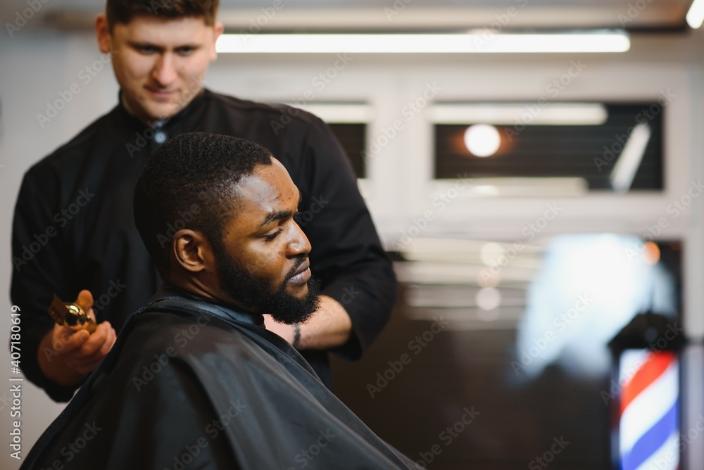 Portrait of young black man being trimmed with professional electric clipper machine in barbershop.Male beauty treatment concept. Young African guy getting new haircut in barber salon Portrait of young black man being trimmed with professional electric clipper machine in barbershop.Male beauty treatment concept. Young African guy getting new haircut in barber salon