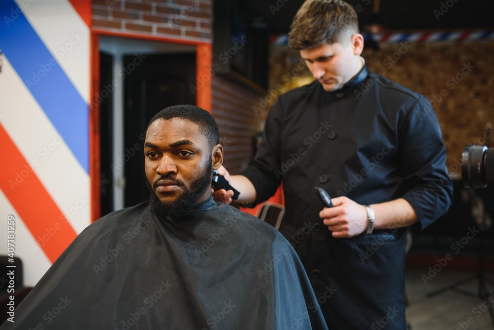 Closeup of process of trimming of hair in barber shop. Qualified barber keeping clipper in hands and correcting shape of hair to male client sitting on chair. Concept of haircut and shaving. Closeup of process of trimming of hair in barber shop. Qualified barber keeping clipper in hands and correcting shape of hair to male client sitting on chair. Concept of haircut and shaving.