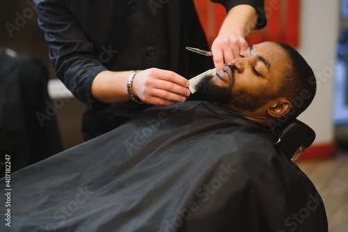 African male client getting haircut at barber shop from professional hairstylist.