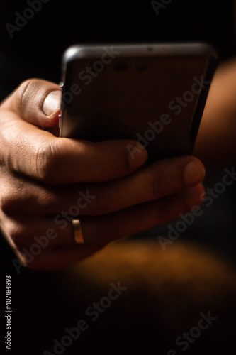 Mobile phone in male hand with wedding ring on finger with blurred background close up