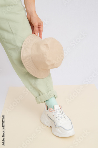 Details of trendy casual spring summer fresh outfit. Girl in studio wearing khaki jeans and stylish white sneakers.  Bucket hat. No face. Minimalist vegan clothing concept