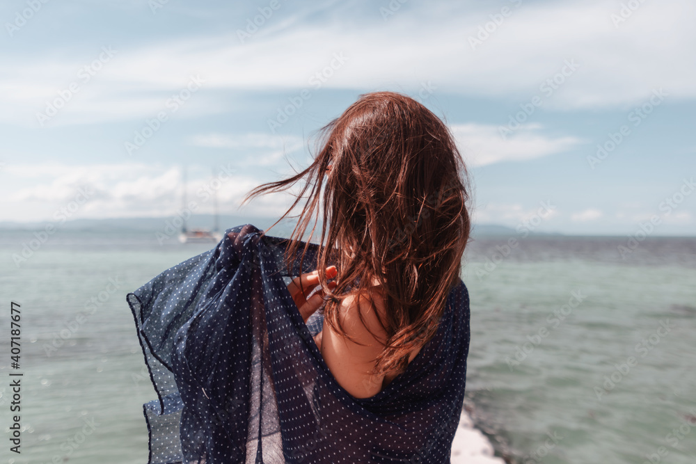 Young woman standing with her back with fluttering hair relaxing by the sea, image with retro toning Young woman standing with her back with fluttering hair relaxing by the sea, image with retro toning