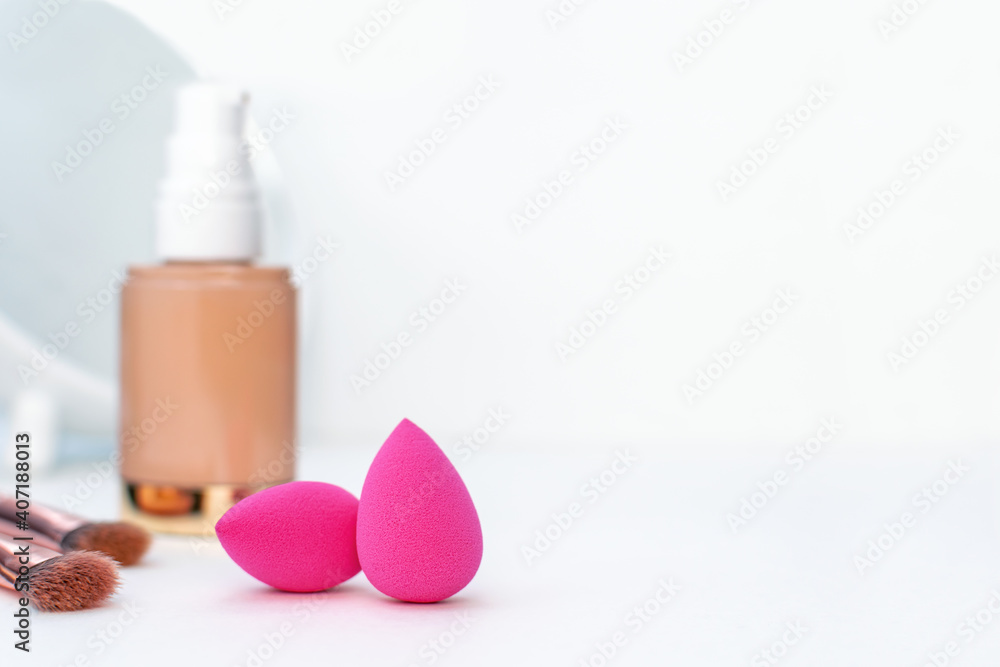Pink sponge and a bottle of beige cosmetic foundation, brushes for make-up and mirror on white table background, close-up. Makeup artist and woman accessories for perfect face skin, beauty, copyspace.