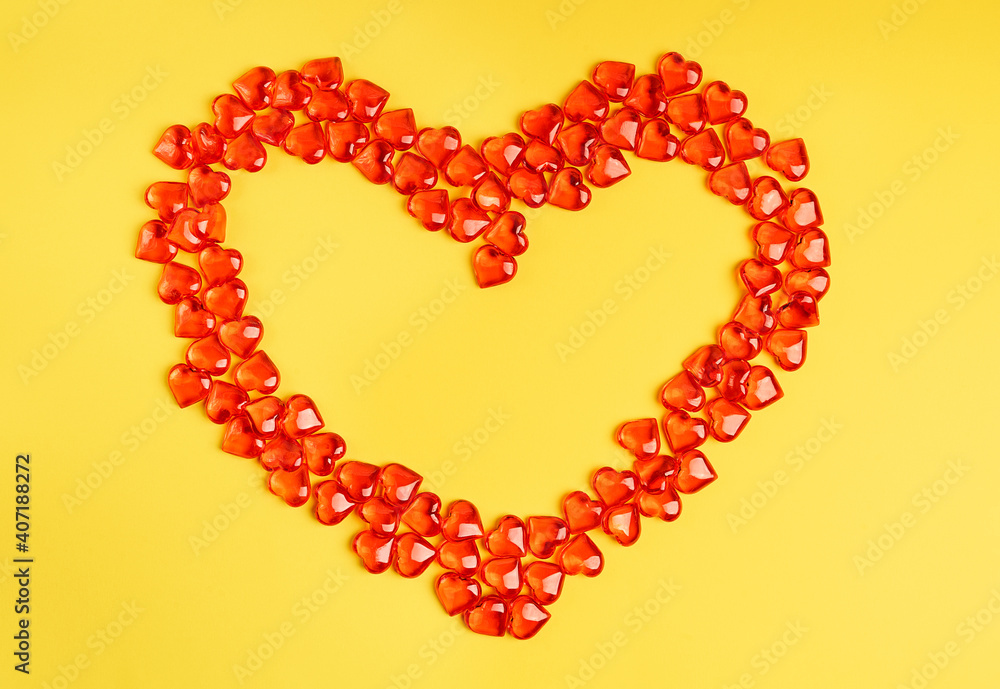 Obraz premium Small red heart shape transparent candies or glass decorations laying on bright vibrant yellow background as a lovely greeting card on saint valentine's day. Image with copy space, horizontal