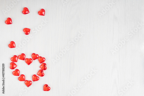 Small red heart shape transparent candies or glass decorations laying on white wooden background as a lovely gift on saint valentine's day. Image with copy space, horizontal