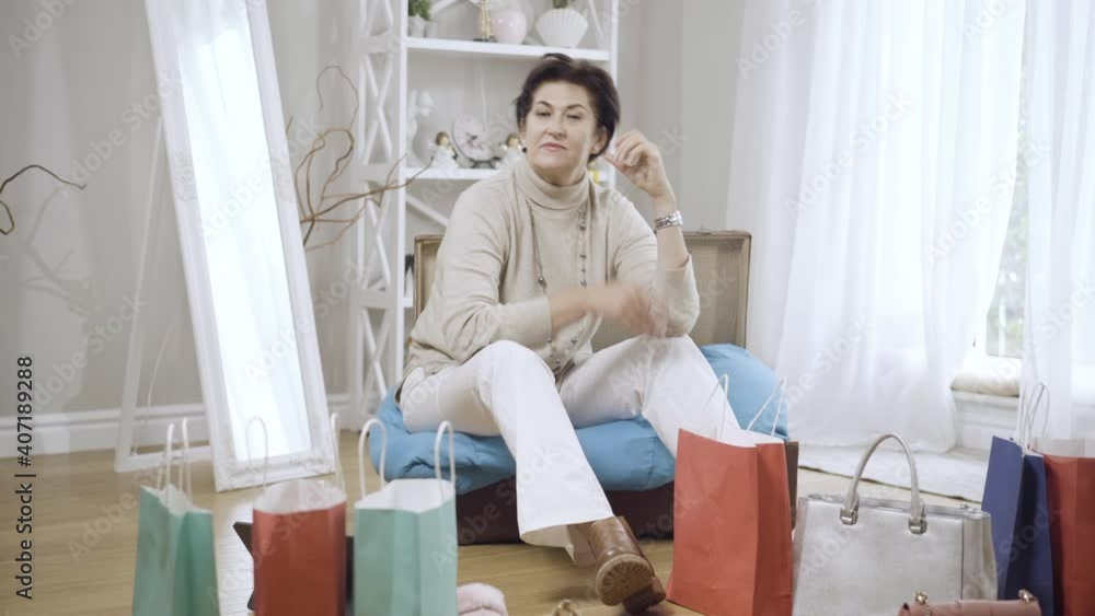 Wide shot of female middle-aged shopaholic with shopping bags looking at camera with desperate facial expression. Sad Caucasian woman regrets on buying purchases on Black Friday. Shopaholism. Wide shot of female middle-aged shopaholic with shopping bags looking at camera with desperate facial expression. Sad Caucasian woman regrets on buying purchases on Black Friday. Shopaholism.