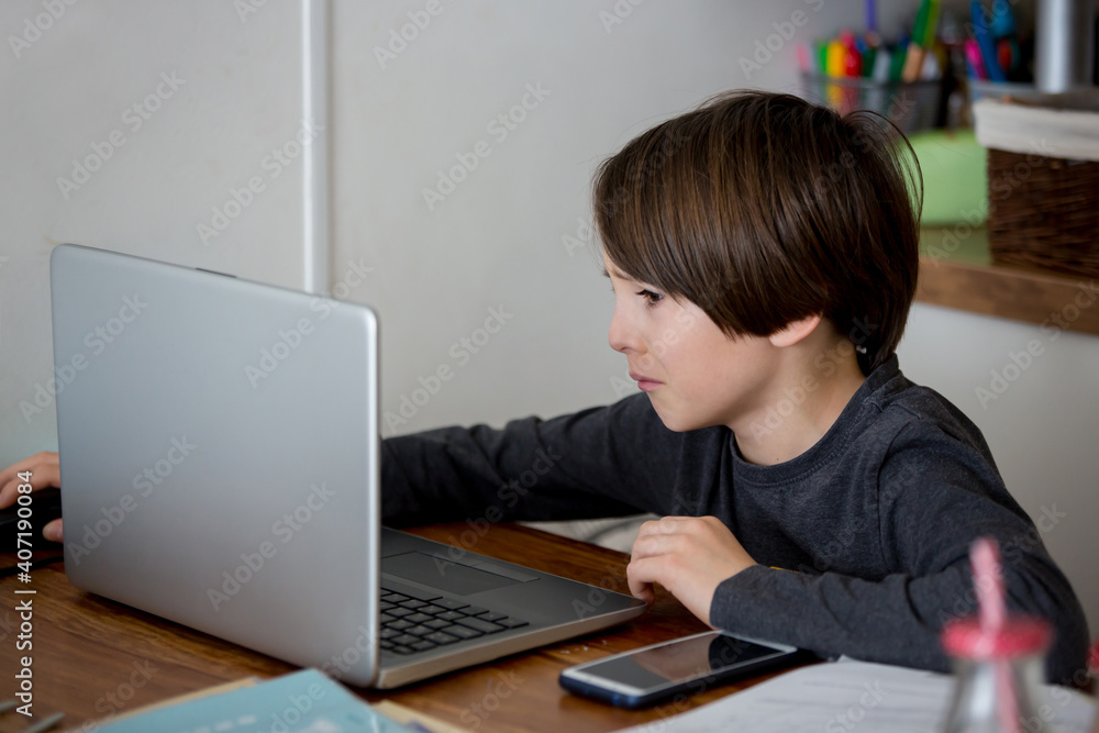 Sad school child, struggling with studying, sitting at the table with laptop, writing school tasks while homeschooling Sad school child, struggling with studying, sitting at the table with laptop, writing school tasks while homeschooling