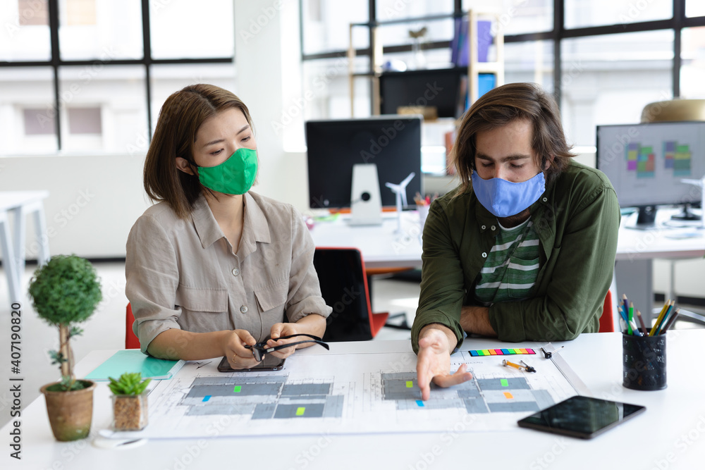 Diverse male and female colleague wearing face masks looking at blueprints and discussing Diverse male and female colleague wearing face masks looking at blueprints and discussing