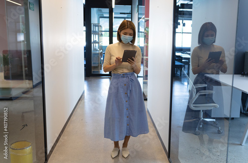Asian businesswoman wearing face mask standing in corridor using tablet