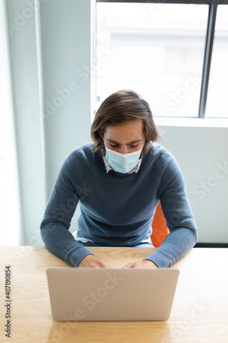 Caucasian businessman wearing face mask sitting at desk using laptop photo