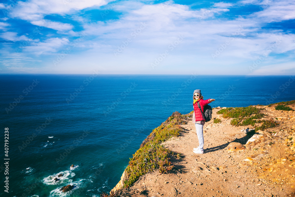 Happy young cheerful woman traveler on the coast of the atlantic ocean in Portugal, Cape Roca