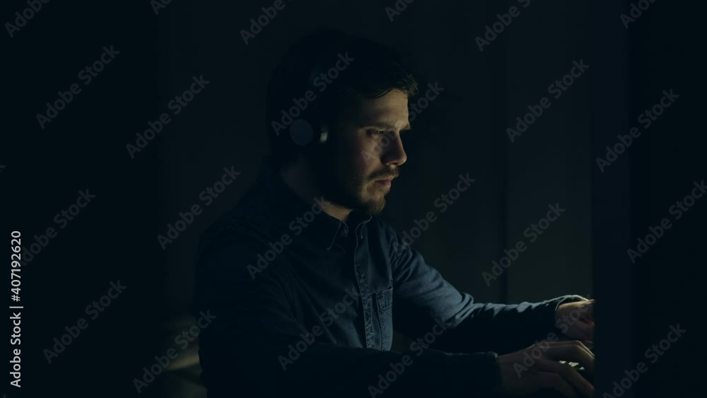 Male Gamer wearing Headphones, playing a Video Game on his Laptop PC in Living Room. Excited Bearded Man is playing Emotional on table at Home in night. Playing Games in Quarantine. Gamers Lifestyle. Male Gamer wearing Headphones, playing a Video Game on his Laptop PC in Living Room. Excited Bearded Man is playing Emotional on table at Home in night. Playing Games in Quarantine. Gamers Lifestyle.