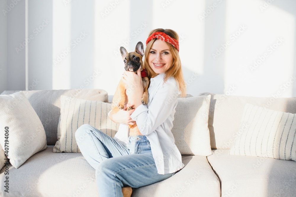 Cheerful young woman holding her big puppy with black nose and laughing. Indoor portrait of smiling girl posing with french bulldog Cheerful young woman holding her big puppy with black nose and laughing. Indoor portrait of smiling girl posing with french bulldog