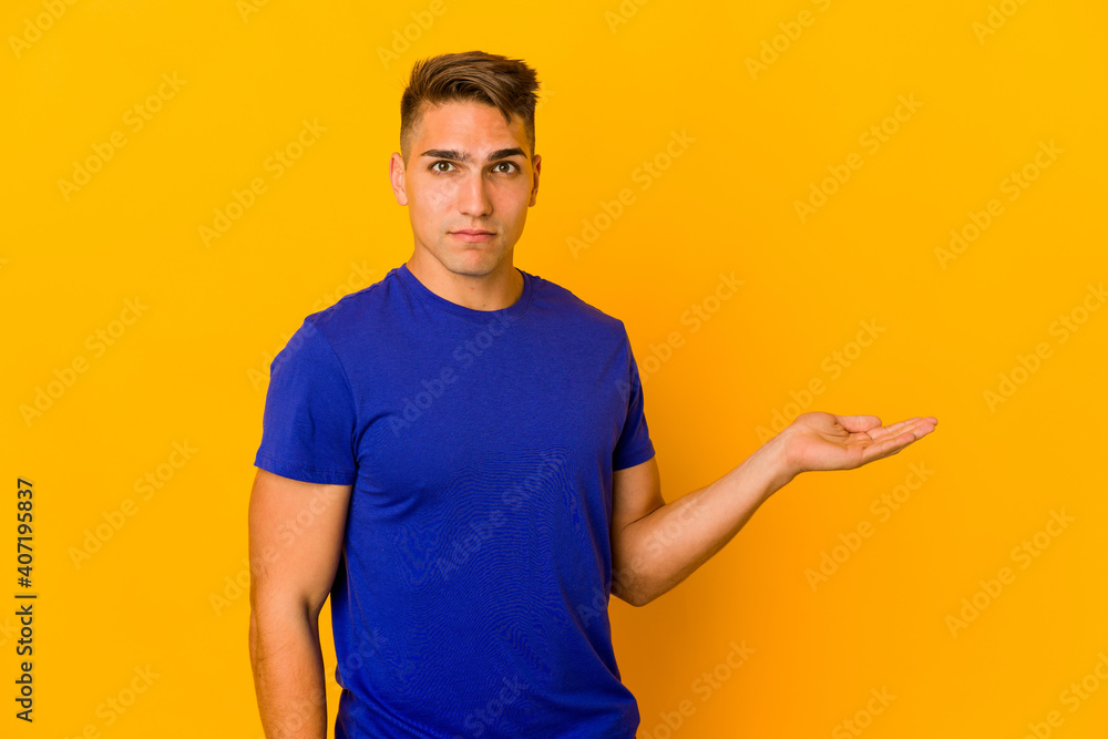 Young handsome caucasian man isolated showing a copy space on a palm and holding another hand on waist. Young handsome caucasian man isolated showing a copy space on a palm and holding another hand on waist.