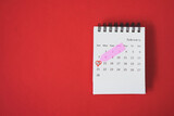 white calendar marked on 14 February with sweet pink arrow and red heart shape around date on grunge red paper background, valentine's day