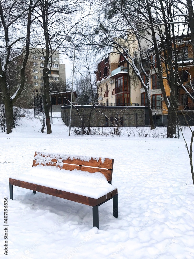 One bench in the snow in a beautiful city winter park against the backdrop of a new urban area, winter landscape One bench in the snow in a beautiful city winter park against the backdrop of a new urban area, winter landscape