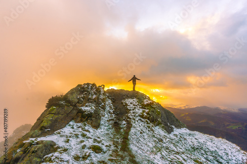 A young man on top of the mountain in the snowy winter orange sunset, on Mount Peñas de Aya in the town of Oiartzun near San Sebastián, Gipuzkoa. Basque Country