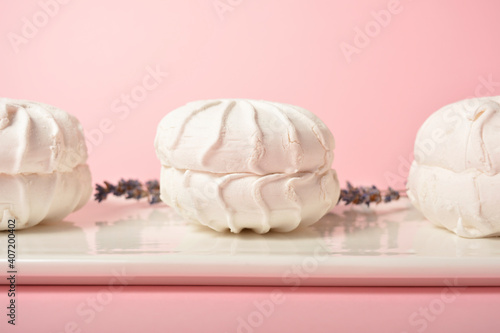 Three Pieces of souffle airy dessert zefir (zephyr) made of organic pectin and egg whites, similarly to marshmallow and meringue. Served on white plate with dry lavender herbs on pastel background
 photo