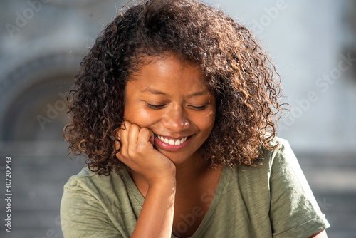 Close up smiling young woman with curly hair relaxing and looking down
