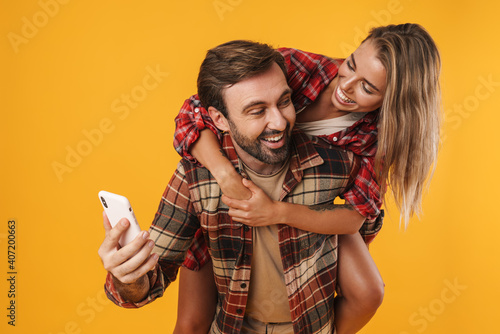 Happy man using cellphone while piggyback riding his smiling girlfriend